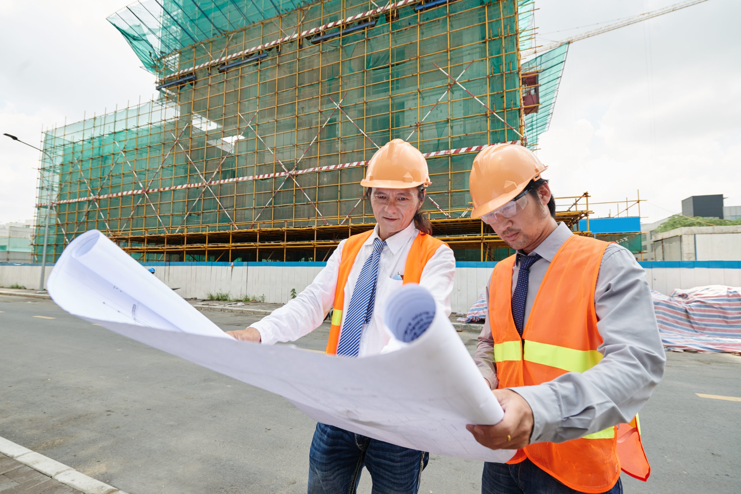 Asian engineers examining plan of building at the construction site