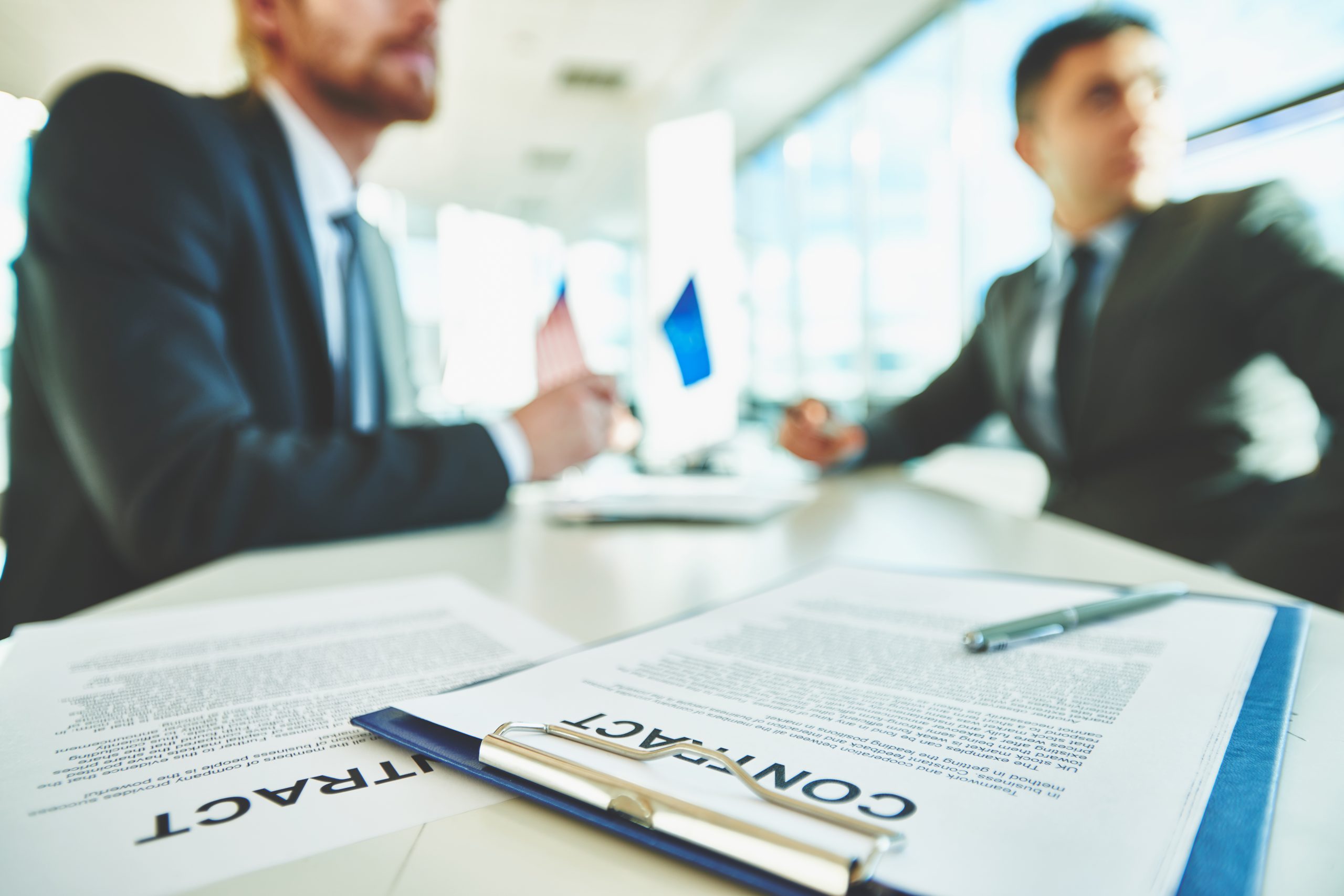 Business contracts on the desk with two male colleagues sitting on background