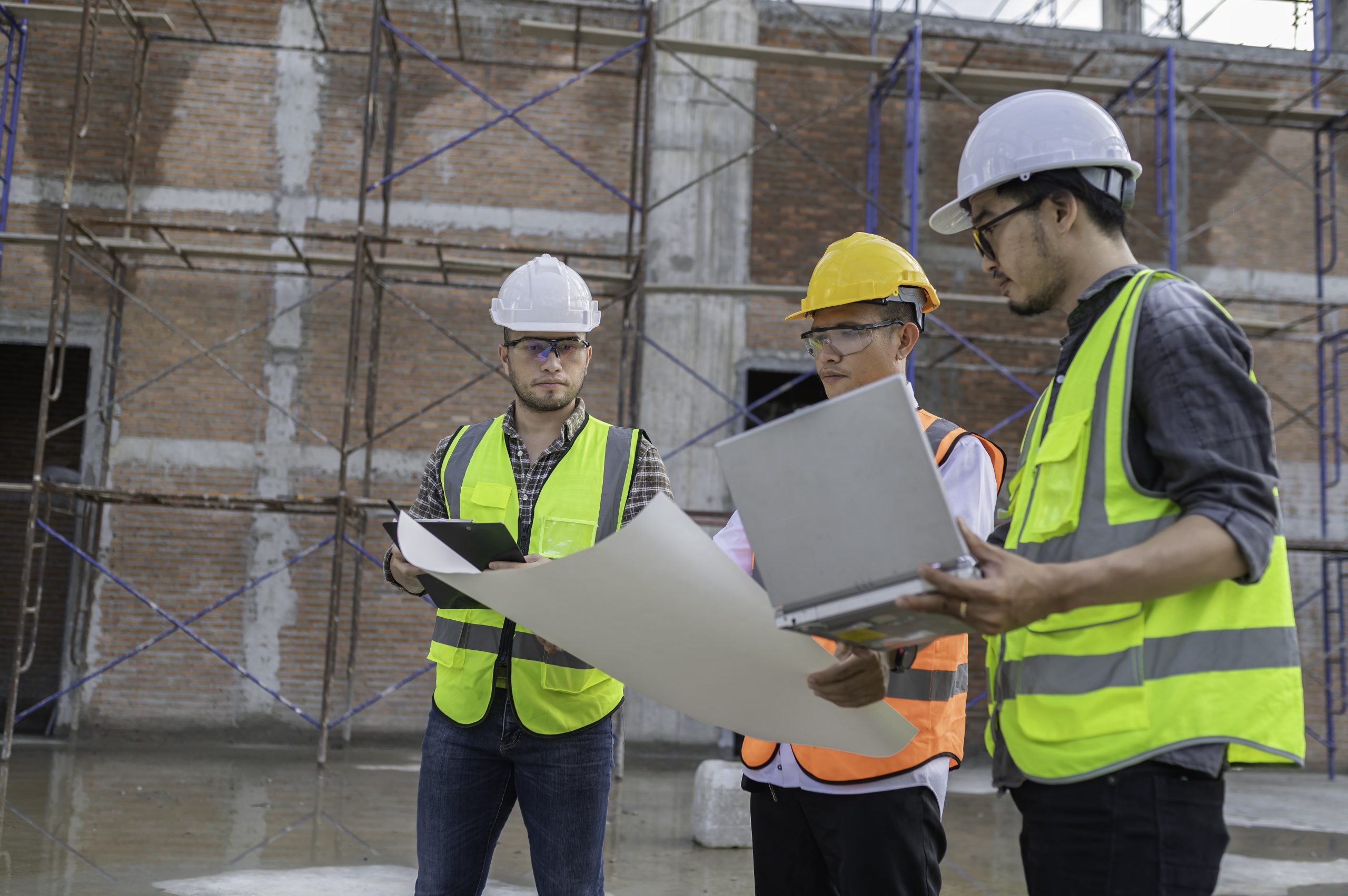 Three Asian engineer working at site of a large building project,Work overtime at construction site,Team of engineer discus at site,The architect, supervisor, and foreman meet to discuss the design